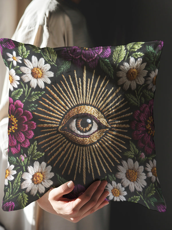Grimoire and Goblet gothic pillow cover featuring a central evil eye surrounded by radiating gold sunburst rays, framed by white daisy flowers, magenta floral blooms, and green botanical foliage on a black background, designed with a highly detailed faux embroidery print that mimics stitched texture while remaining smooth, arranged in a symmetrical medallion composition, creating a dark academia and witchy botanical aesthetic decorative cushion cover