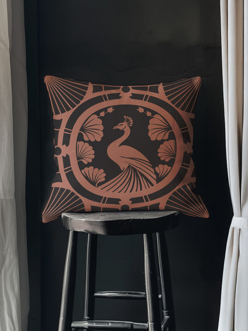 Square pillow cover featuring a stylized copper peacock design centered in a medallion, surrounded by Art Deco fan patterns and shell motifs on a dark forest green background.