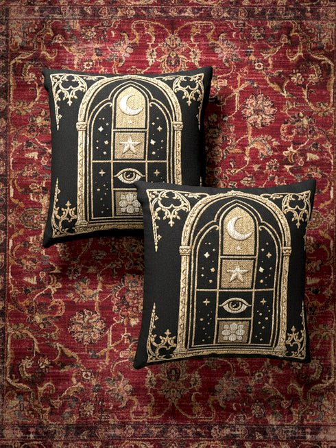 Woven jacquard throw pillow by Grimoire and Goblet featuring a gothic cathedral arch window design in black and gold. Central motifs include a waxing crescent moon, a five-pointed celestial star, a protective all-seeing eye, and a blooming botanical flower. Texture is raised tapestry weave, not printed. Perfect for dark academia, whimsigoth, and witchy home decor styles. Black background with beige and ochre accents. Square shape 17x18 inches.