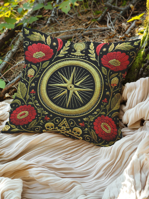 A square Grimoire and Goblet throw pillow cover featuring a high-contrast Dark Academia design. The background is deep black, highlighting a central gold compass rose medallion surrounded by a circular border. Flanking the compass are large crimson red poppy flowers with gold centers and intricate green and gold leafy foliage in a faux embroidery style. The bottom center features small gold skulls and crossbones with a triangle symbol. The texture is printed illusion of tapestry threadwork.