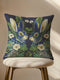 A Grimoire and Goblet decorative throw pillow cover featuring a high-fidelity print of two symmetrical hares facing each other. The design mimics the texture of raised embroidery with faux-stitches in antique gold, ochre, and royal blue threads against a deep midnight indigo background. The rabbits are surrounded by a lush wreath of green ferns and cream primrose flowers in a vintage medallion style. The fabric has a smooth, linen-like texture, visible as a soft matte finish