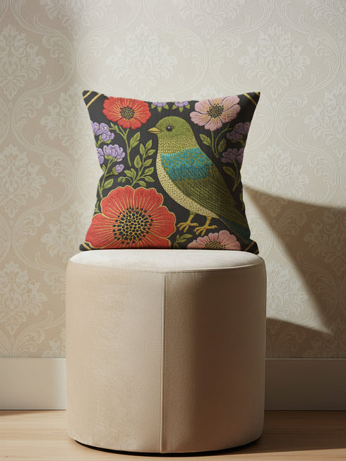 Square decorative pillow cover with a near-black ground and a richly colored Art Nouveau botanical design rendered in a faux embroidery style. At the center perches a songbird with an olive and chartreuse body, a teal wing patch, and golden-yellow beak and feet. Around it bloom large red-orange poppies with golden centers, clusters of lilac and lavender flowers, and pale pink daisy-like blossoms among green leaves. The printed satin-stitch detailing mimics dense hand embroidery across the cover.