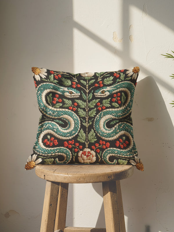 Grimoire & Goblet faux embroidery serpent pillow cover featuring two mirrored teal and cream snakes on a charcoal black background with red berries, green botanical leaves, daisy flowers, and a central floral motif. Printed textile illusion artwork with stitched embroidery look, double-sided design, hidden zipper closure, and linen-like polyester finish. Gothic botanical throw pillow cover for dark academia, witchy, Victorian-inspired home decor.