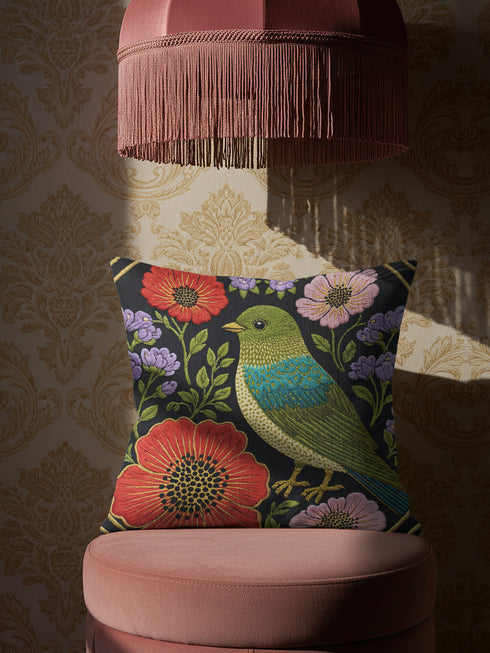 Square decorative pillow cover with a near-black ground and a richly colored Art Nouveau botanical design rendered in a faux embroidery style. At the center perches a songbird with an olive and chartreuse body, a teal wing patch, and golden-yellow beak and feet. Around it bloom large red-orange poppies with golden centers, clusters of lilac and lavender flowers, and pale pink daisy-like blossoms among green leaves. The printed satin-stitch detailing mimics dense hand embroidery across the cover.