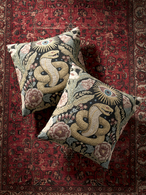 Grimoire and Goblet Celestial Serpent woven tapestry pillow close up. A luxurious black jacquard cushion features a golden coiled snake and All-Seeing Eye surrounded by sage green foliage and stars. The texture is thick and woven, not printed. The serpent scales shimmer in gold thread against a dark charcoal background. Double sided Gothic home decor pillow measuring 17x18 inches. Perfect for Dark Academia, Whimsigoth living rooms, and Year of the Snake 2025 decor.
