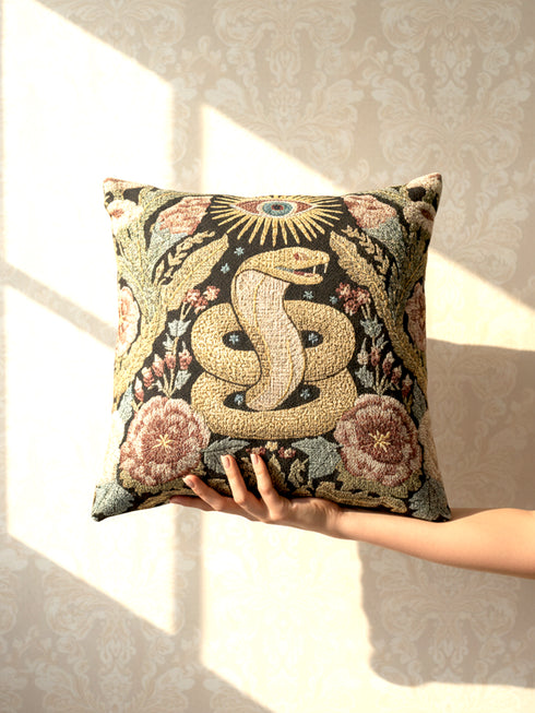 Grimoire and Goblet Celestial Serpent woven tapestry pillow close up. A luxurious black jacquard cushion features a golden coiled snake and All-Seeing Eye surrounded by sage green foliage and stars. The texture is thick and woven, not printed. The serpent scales shimmer in gold thread against a dark charcoal background. Double sided Gothic home decor pillow measuring 17x18 inches. Perfect for Dark Academia, Whimsigoth living rooms, and Year of the Snake 2025 decor.