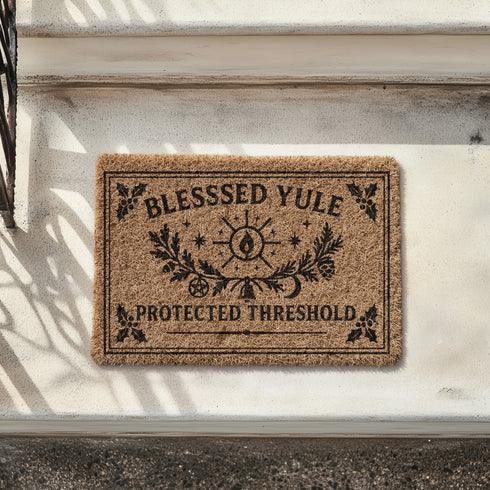 A rectangular tufted coir doormat with a non-slip black vinyl backing, features an intricate gothic botanical design in black. At the top, it reads "BLESSED YULE" with holly motifs in the corners. In the center, a laurel wreath, intertwined with a pentacle and a bell, encircles a radiant candle. Below the wreath rests a pinecone. At the bottom, the text "PROTECTED THRESHOLD" is flanked by holly. This pagan and witchy Grimoire and Goblet design is perfect for a gothic or dark academia entryway.