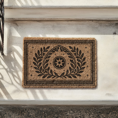 A rectangular natural coir doormat with a durable, non-slip black vinyl backing. The surface features an intricate black gothic-style design centered around an eight-pointed celestial star. This mystical symbol is encircled by a pointed arch formed from two botanical laurel branches, symbolizing wisdom and protection. The central motif is framed by a double border with geometric details and smaller stars. A perfect piece of spiritual home decor for a pagan or mystical entryway.