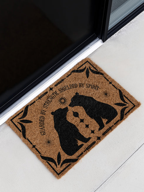 Natural coir doormat featuring two black bear silhouettes facing each other, surrounded by botanical and celestial accents. The mat is made from eco-friendly coir fiber with a slip-resistant vinyl backing, ideal for outdoor use in covered entryways.
