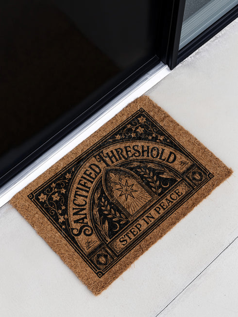 Threshold Doormat featuring a black Gothic arched doorway design on natural tan coir. The design includes a central eight-pointed star sunburst octagram symbol inside the arch, flanked by symmetrical laurel branches and corner ivy vine filigree. This 24x16 protective threshold mat is made of eco-friendly coconut fiber with a stable black vinyl backing. Ideal as a witchy housewarming gift or dark academia entry rug, this warding mat functions as a symbolic threshold guardian for a mystical home.