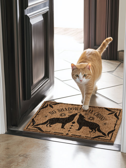 Natural coir doormat featuring black silhouettes of two howling wolves in symmetrical formation, surrounded by celestial and botanical details. The phrase No Shadows May Cross is hand-stenciled above, with a non-slip vinyl backing for outdoor use.