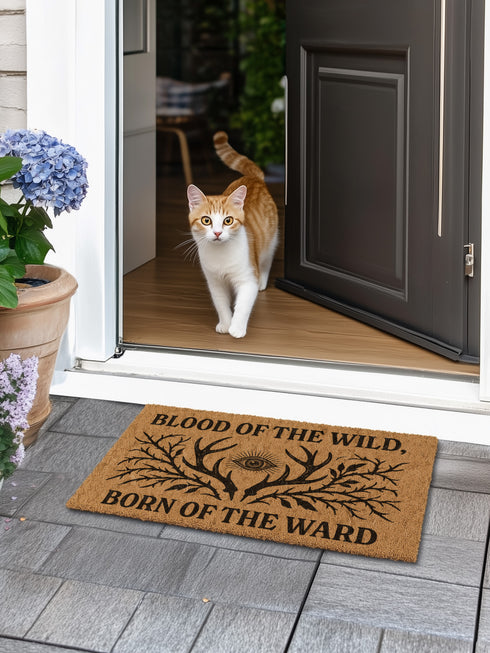 Rectangular coir doormat measuring 24x16 inches featuring black printed text reading “Blood of the Wild, Born of the Ward” with an all-seeing eye symbol and antler-branch illustration. Made from natural coconut fiber with a durable black vinyl backing, this outdoor doormat is weather-resistant and ideal for gothic, witchy, or folklore-inspired entryways.