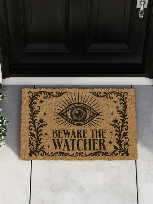 Coir doormat printed with “Beware the Watcher” in black ink, featuring a central all-seeing eye, ornate floral border, and star accents. Shown on outdoor stairs and entryways. Made from natural coconut fiber with black vinyl backing. A bold, mystical gift for witches, goth home lovers, and spiritual housewarmings.