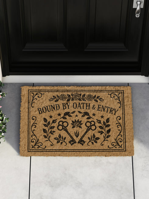A rectangular, tufted coir doormat in a natural tan coconut fiber, shown flat from a top-down perspective. The detailed design, printed in stark black ink, features the capitalized words 'BOUND BY OATH & ENTRY' in an elegant, old-world serif font. Below the text, two antique-style skeleton keys are crossed, their ornate heads pointing outwards. The keys are flanked by leafy botanical branches. A central lotus-like rose and small stars accent the design, Victorian-style filigree border.
