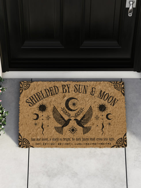 Natural coir doormat featuring two symmetrical doves beneath a crescent moon, surrounded by celestial and botanical accents. The phrase Shielded by Sun & Moon is stenciled above, with a protective incantation at the base. Non-slip vinyl backing for outdoor use.
