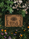 Coir doormat printed with “Beware the Watcher” in black ink, featuring a central all-seeing eye, ornate floral border, and star accents. Shown on outdoor stairs and entryways. Made from natural coconut fiber with black vinyl backing. A bold, mystical gift for witches, goth home lovers, and spiritual housewarmings.