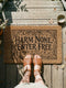 A rectangular natural coir doormat featuring the Wiccan Rede "An' It Harm None, Do What Ye Will" in a gothic dark academia style. The central typography is surrounded by symmetrical botanical flourishes and mystical symbols printed in high-contrast black ink. The 2D flat print mimics the look of a vintage grimoire page on the coarse, tan coconut fiber surface. The mat has a durable black vinyl backing and is pictured at a front door as a protective threshold guardian.