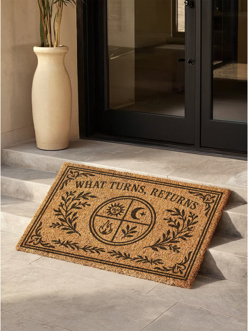 Natural coir doormat featuring "What Turns, Returns" text with sacred elemental symbolism including sun, crescent moon, flames, and botanical sprigs arranged in protective circular mandala design. Four classical elements represented in quadrants surrounded by intricate corner flourishes and leafy botanical borders. Perfect witchy welcome mat for pagan home decor, spiritual protection, and mystical entryway styling.