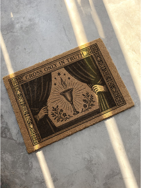 A rectangular doormat made from natural, textured brown coir fiber, featuring a striking black gothic design for spiritual threshold protection. The centerpiece of this witchy welcome mat is a sacred flaming chalice, set between two parted curtains for a dramatic entryway statement. Above the occult imagery, the phrase 'Cross Only In Truth' is printed in a mystical font reminiscent of ancient spellbooks, making this metaphysical and dark academia decor a powerful symbol for a protected home. This is a doorm