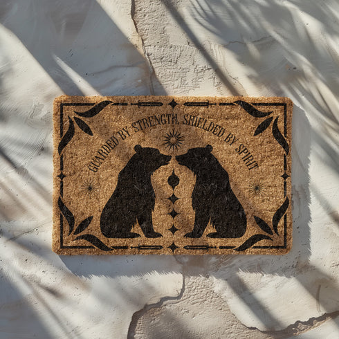 Natural coir doormat featuring two black bear silhouettes facing each other, surrounded by botanical and celestial accents. The mat is made from eco-friendly coir fiber with a slip-resistant vinyl backing, ideal for outdoor use in covered entryways.