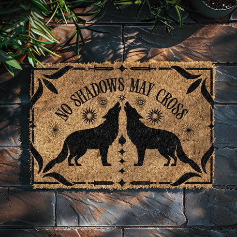 Natural coir doormat featuring black silhouettes of two howling wolves in symmetrical formation, surrounded by celestial and botanical details. The phrase No Shadows May Cross is hand-stenciled above, with a non-slip vinyl backing for outdoor use.