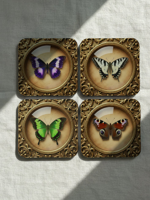 Grimoire and Goblet offers this luxury four-piece square Coaster Set featuring glossy, dome-covered, Taxidermy-inspired Entomology butterfly specimens, framed in ornate Victorian Gothic style. The resilient hardboard foundation and non-slip cork backing provide premium, waterproof protection for fine cocktails and esoteric teas. The collection includes purple, green, white, and peacock butterfly art, ideal for Dark Academia, Oddity, and Curio Cabinet decor.