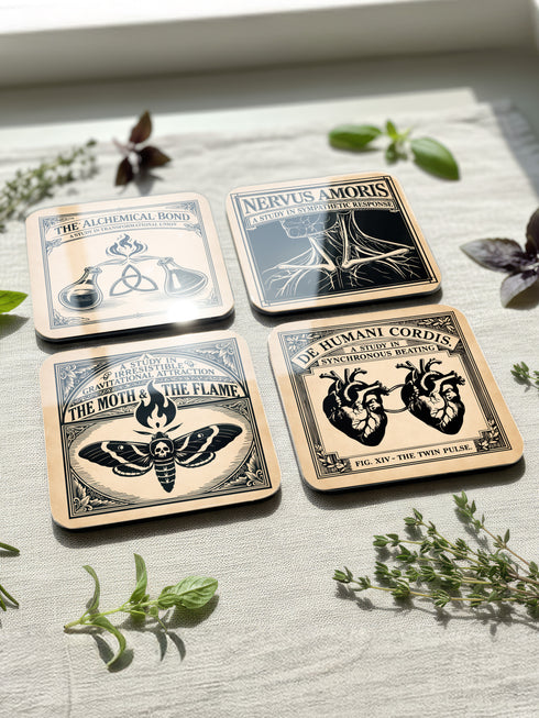 Set of four 4-inch square anatomical love coasters by Grimoire and Goblet. Each coaster features a black ink illustration on an antique tan parchment background in a Victorian scientific style. Designs include linked anatomical hearts for "De Humani Cordis," a triquetra and alchemy flasks for "The Alchemical Bond," a Death's Head moth for "The Moth & The Flame," and a study of neck nerves for "Nervus Amoris." Ideal for a Victorian grimoire aesthetic and gothic romance home bar decor.