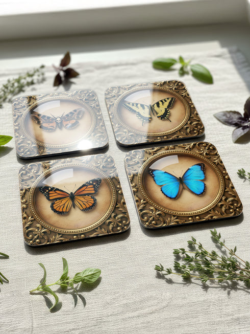 Set of four Gothic Entomology Coasters featuring square, ornate gold frames surrounding taxidermy-inspired butterfly and moth specimen prints in high-gloss finish. Ideal barware from Grimoire and Goblet for Dark Academia and witchy home decor.