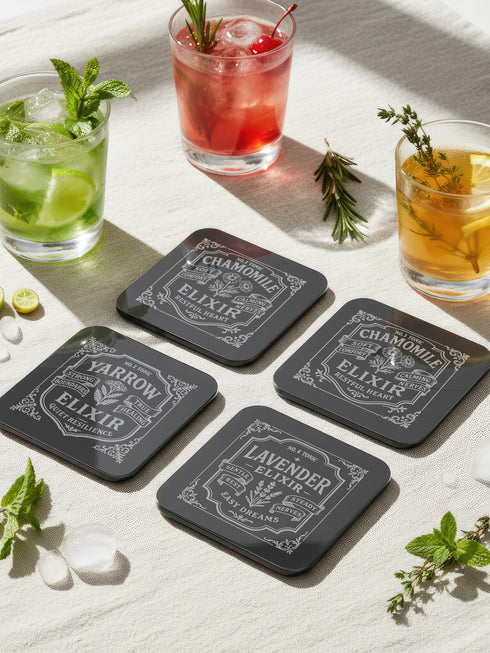 A complete set of four square, black, gloss beverage coasters with protective cork bases. Each coaster features an intricate Art Nouveau botanical design in white, stylized as a vintage elixir label. The set includes distinct labels for Sage, Chamomile, Yarrow, and Lavender, each inscribed with positive affirmations relating to healing and inner balance. These elegant Gothic drinkware pieces are designed to complement Dark Academia and Whimsigoth home decor, reflecting the arcane aesthetic.