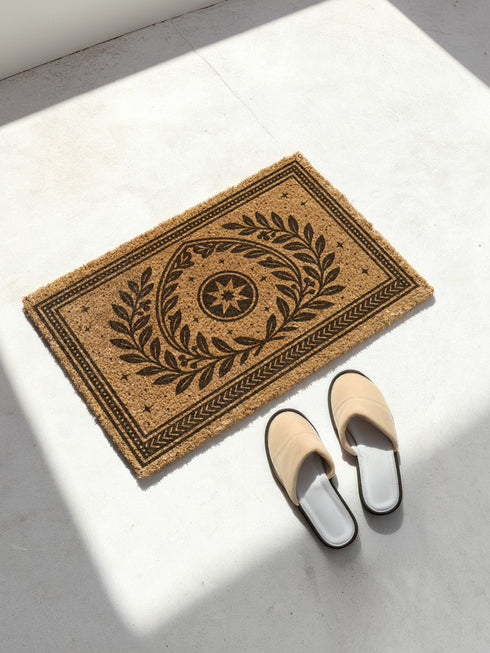A rectangular natural coir doormat with a durable, non-slip black vinyl backing. The surface features an intricate black gothic-style design centered around an eight-pointed celestial star. This mystical symbol is encircled by a pointed arch formed from two botanical laurel branches, symbolizing wisdom and protection. The central motif is framed by a double border with geometric details and smaller stars. A perfect piece of spiritual home decor for a pagan or mystical entryway.