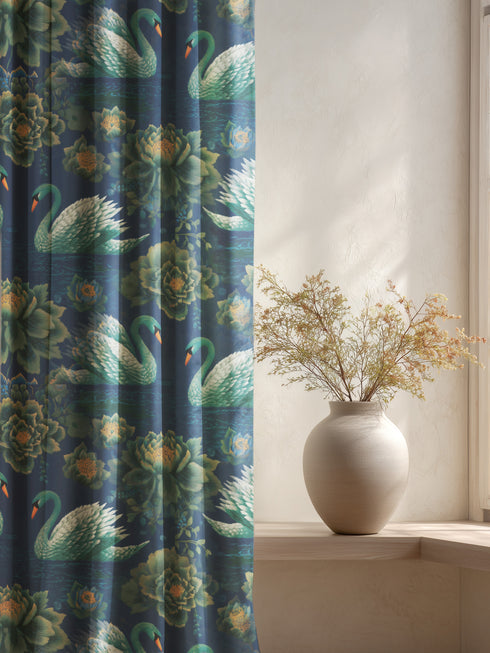 Grimoire and Goblet blackout curtain panel featuring a repeating Art Nouveau pattern of regal white swans and lush emerald green peonies on a deep midnight navy blue background. The design includes floating lily pads and stylized floral foliage with hints of ochre gold. The fabric is 100% heavyweight polyester with a satin finish and a rod pocket header. The print mimics the look of vintage embroidery but is a smooth, high-quality flat print.