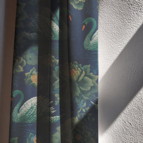Grimoire and Goblet blackout curtain panel featuring a repeating Art Nouveau pattern of regal white swans and lush emerald green peonies on a deep midnight navy blue background. The design includes floating lily pads and stylized floral foliage with hints of ochre gold. The fabric is 100% heavyweight polyester with a satin finish and a rod pocket header. The print mimics the look of vintage embroidery but is a smooth, high-quality flat print.