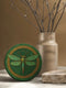 Round ceramic coaster featuring a raised gold-tone dragonfly relief and ornate border on a deep green glazed surface; 4-inch diameter; backed with natural cork for non-slip stability; heat- and cold-resistant; easy-wipe ceramic top; ideal for mystical, botanical, or occult-inspired tabletops.