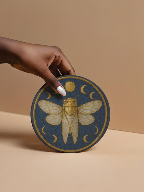 Round ceramic coaster featuring a central gold cicada and moon-phase design on a deep blue glazed surface; smooth ceramic top with natural cork backing for non-slip protection; 4-inch diameter, suitable for hot or cold drinks, easy to wipe clean, ideal for mystical, botanical, or occult-inspired home décor.