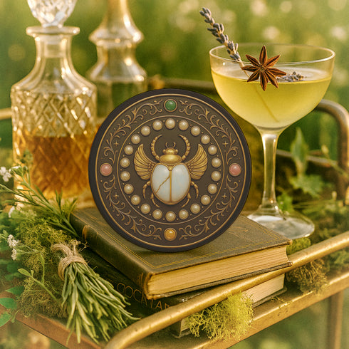 Round ceramic coaster with a cork backing, featuring an ornate scarab beetle design surrounded by gold scrollwork, pearls, and gemstone accents in a circular motif.