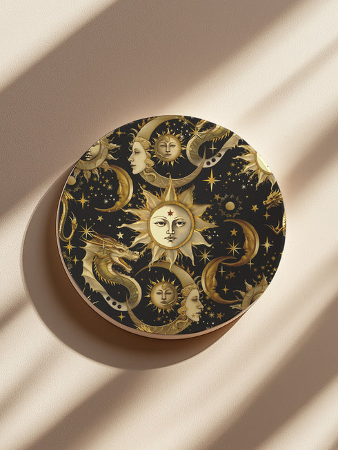 A round ceramic coaster featuring a dark navy background with golden celestial design elements: baroque-style sun faces, crescent moons with feminine profiles, stars, and a mystical dragon. The pattern is rendered in metallic gold tones, creating a rich, ornate astronomical motif.