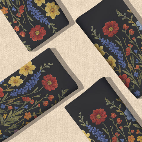 Four-piece cloth napkin set featuring a richly embroidered-style wildflower motif on a deep black background. Includes yellow, red, blue, and orange florals with intricate green stems and leaves. Each napkin is printed on one side and measures 18 x 18 inches, made from smooth polyester fabric with white backing.