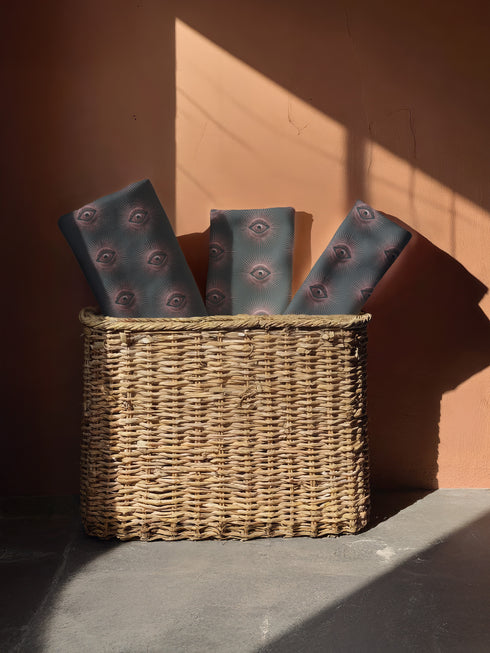 Set of four teal-colored dining napkins featuring a captivating pattern of protective evil eye symbols in dusty rose pink with radiating white lines. Each napkin displays numerous evil eyes arranged in a repeating pattern across the entire surface. The eyes have a vintage, almost Art Deco quality with their symmetrical rays emanating outward like sunbursts. The teal background creates a rich, moody contrast against the rose-pink eyes, giving these napkins a sophisticated, mystical appearance.