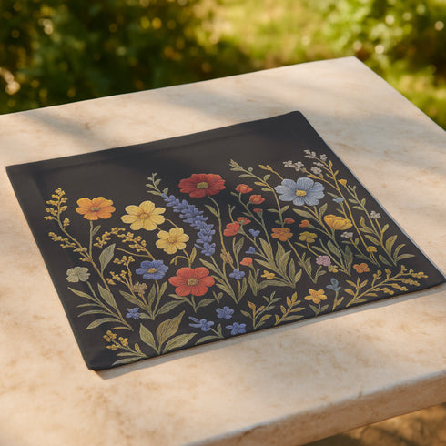 Four-piece cloth napkin set featuring a richly embroidered-style wildflower motif on a deep black background. Includes yellow, red, blue, and orange florals with intricate green stems and leaves. Each napkin is printed on one side and measures 18 x 18 inches, made from smooth polyester fabric with white backing.
