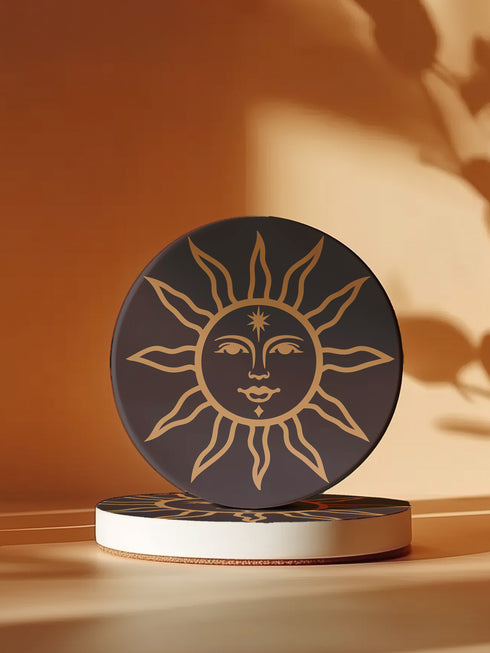 Round ceramic coaster featuring a celestial sun design in warm golden tones against a deep matte black background. The intricate illustration showcases a serene sun face with delicate detailing, surrounded by radiant, curved rays. The smooth, durable surface is complemented by a cork backing for grip and protection, making it both a functional and decorative piece for any space.