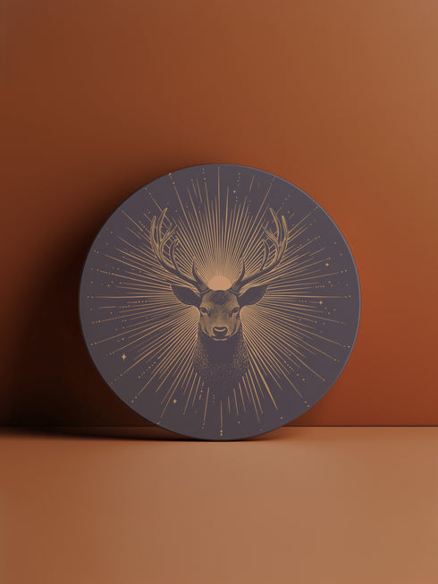 Ceramic coasters in round and square shapes featuring a detailed deer head with branching antlers on a deep navy background. Metallic gold sunburst rays radiate from behind the deer, with scattered stars throughout the design. Each coaster has a protective cork backing.