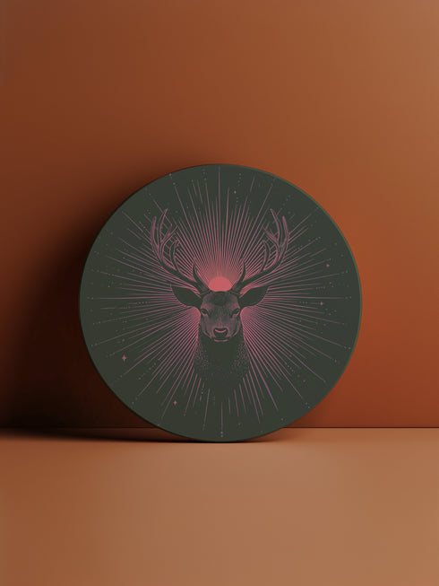 Ceramic coasters in round and square shapes featuring a detailed deer head with majestic antlers against a deep forest green background. A pink-tinged radiant sunburst pattern emanates from behind the deer's head, with delicate stars scattered throughout the design. Cork backing protection.