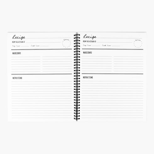 A black spiral-bound hardcover grimoire titled "Spells of Salt & Flame." The cover features an intricate, metallic-effect printed design in silver and gold with an All-Seeing Eye in an archway, flanked by a spoon and an athame. Botanical elements like garlic and herbs grow from a central chalice. The side borders are lined with celestial moon phase symbols. The journal is open, showing blank recipe template pages with fields for ingredients and instructions. The book measures 8.5 x 11 inches.