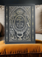 A black spiral-bound hardcover grimoire titled "Spells of Salt & Flame." The cover features an intricate, metallic-effect printed design in silver and gold with an All-Seeing Eye in an archway, flanked by a spoon and an athame. Botanical elements like garlic and herbs grow from a central chalice. The side borders are lined with celestial moon phase symbols. The journal is open, showing blank recipe template pages with fields for ingredients and instructions. The book measures 8.5 x 11 inches.