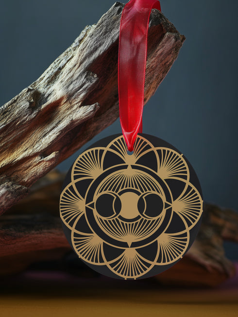 Round metal ornament featuring golden triple moon symbol surrounded by Art Deco sunburst pattern on black background. 3.5-inch diameter piece with symmetrical lunar design and crimson ribbon. Detailed celestial artwork adorns both side