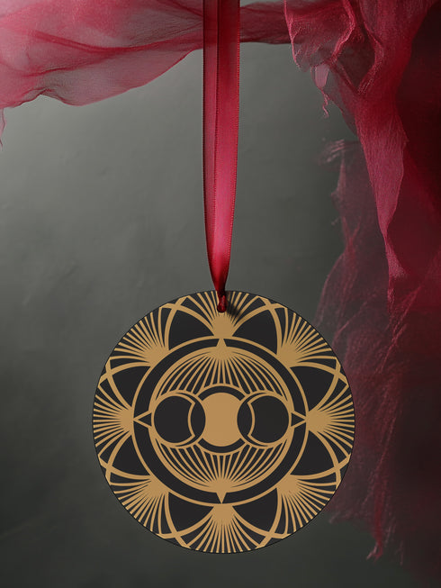 Round metal ornament featuring golden triple moon symbol surrounded by Art Deco sunburst pattern on black background. 3.5-inch diameter piece with symmetrical lunar design and crimson ribbon. Detailed celestial artwork adorns both side