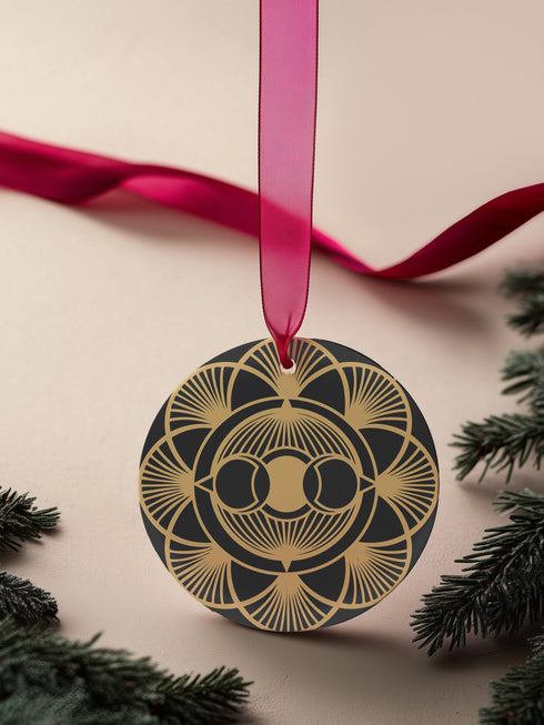 Round metal ornament featuring golden triple moon symbol surrounded by Art Deco sunburst pattern on black background. 3.5-inch diameter piece with symmetrical lunar design and crimson ribbon. Detailed celestial artwork adorns both side