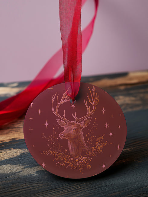 Round metal ornament featuring detailed rose gold etching of a stag's profile with antlers, surrounded by winter foliage and stars on burgundy background. 3.5-inch diameter piece with crimson ribbon. Double-sided woodland artwork.