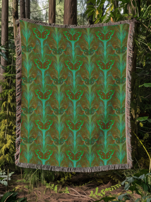 A woven cotton throw featuring an intricate luna moth design in deep green and russet tones, framed by soft fringe.
