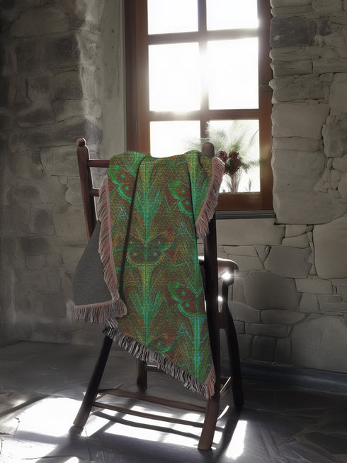A woven cotton throw featuring an intricate luna moth design in deep green and russet tones, framed by soft fringe.